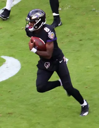 Lamar Jackson running on the field, scoring a touchdown against the Cincinnati Bengals, showcasing his speed and agility, with a crowd of cheering fans in the background.